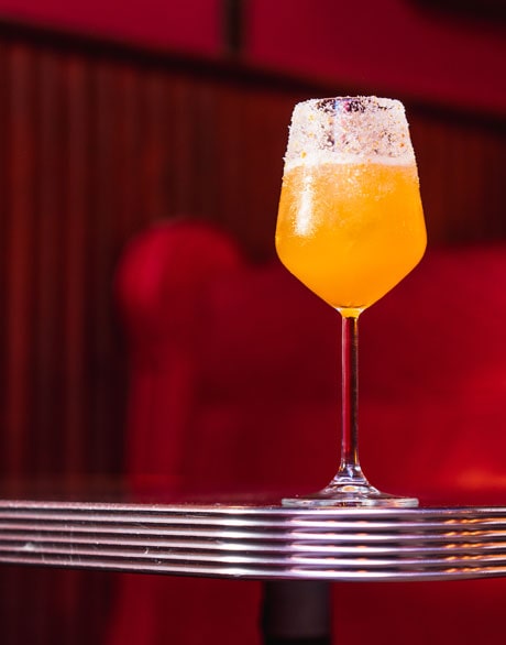 Orange-coloured cocktail in wine glass on diner style table at Stella Steakhouse with red booth seat in background